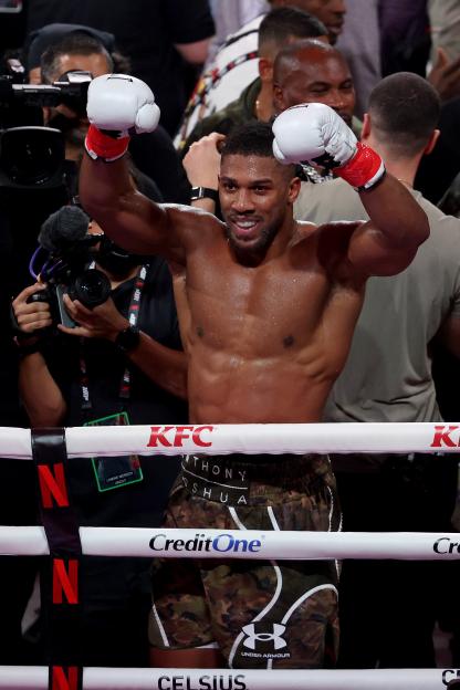 Anthony Joshua celebrates victory with arms raised in a boxing ring.