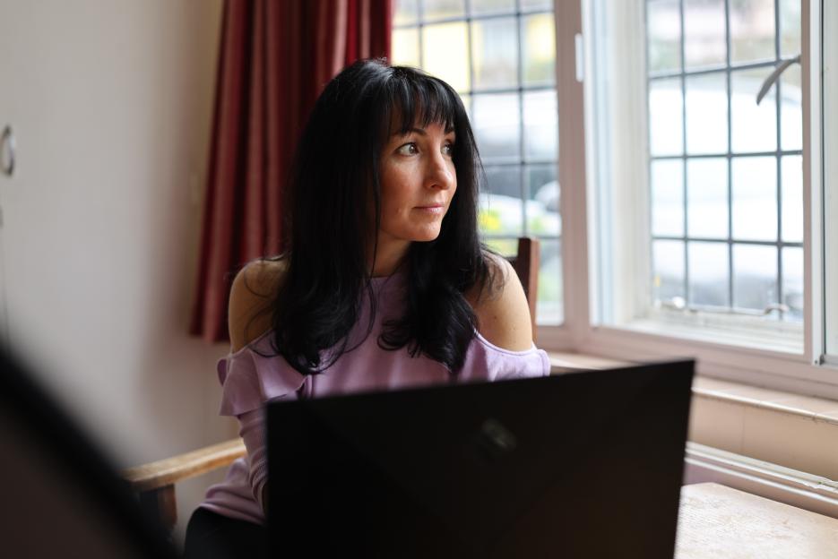 Kirsty Pellant sits in a chair next to a window, looking out to the right.