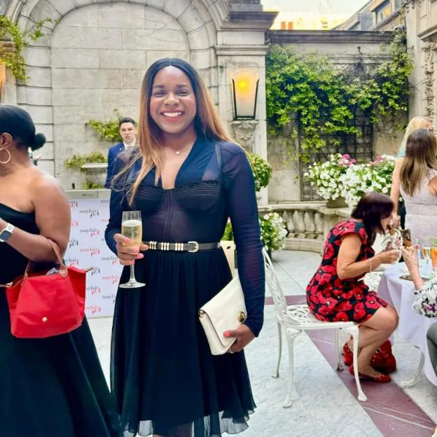Simone de Gale smiling while holding a glass of champagne at an outdoor event.