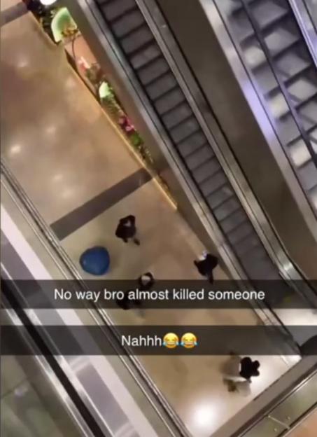A bird's-eye view of a blue object on the ground floor of a mall near an escalator.