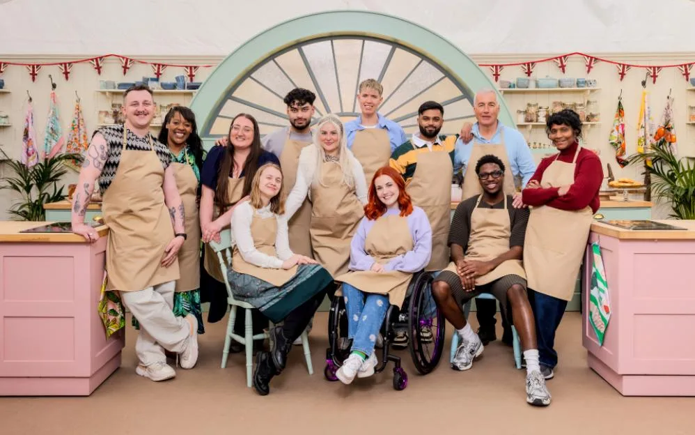 The Great British Bake Off Series 17 contestants (Gabe, Nikki, Shannon, Danni, Mo, Clara, Tom, Molly, Yannis, Gary, Moyin, and Connie) pose for a group photo in the Bake Off tent.