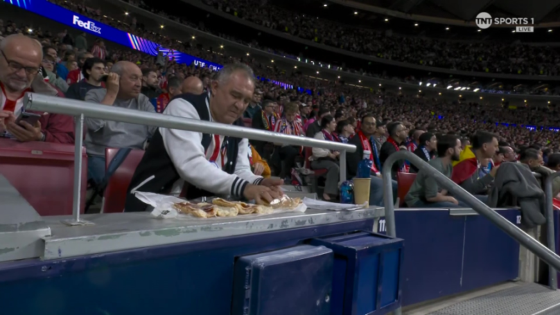 A man in a baseball jacket preparing sandwiches at a sports stadium.