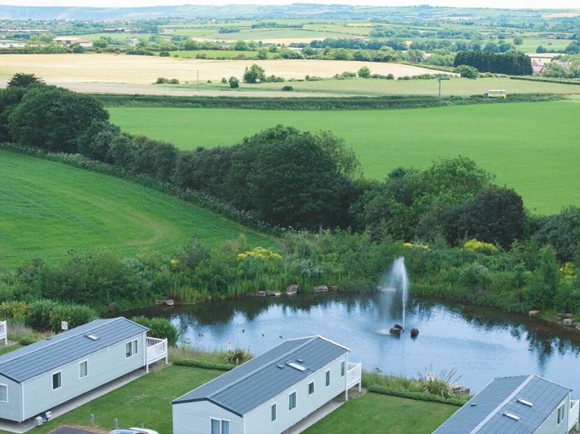 Overview of Blue Dolphin Holiday Park in Yorkshire, showing caravans, a pond with a fountain, and green fields extending into the distance.