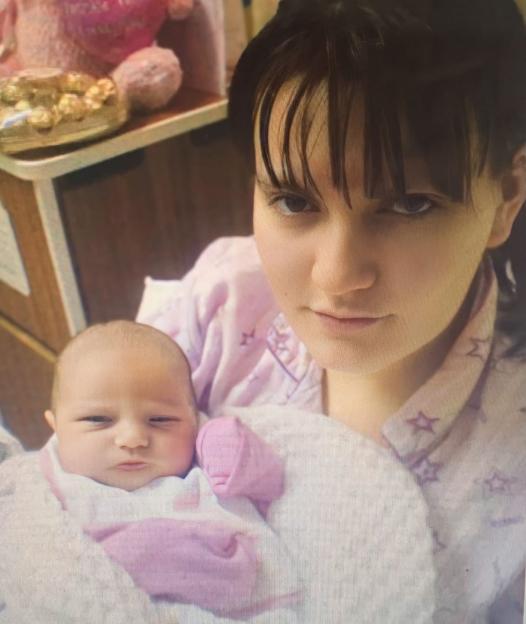 A young woman holding a newborn baby, with a teddy bear and chocolates in the background.
