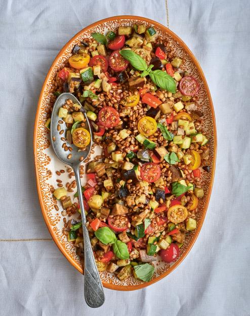 Farro grain dish with diced tomatoes, zucchini, eggplant, and basil, served on an oval plate with a spoon.