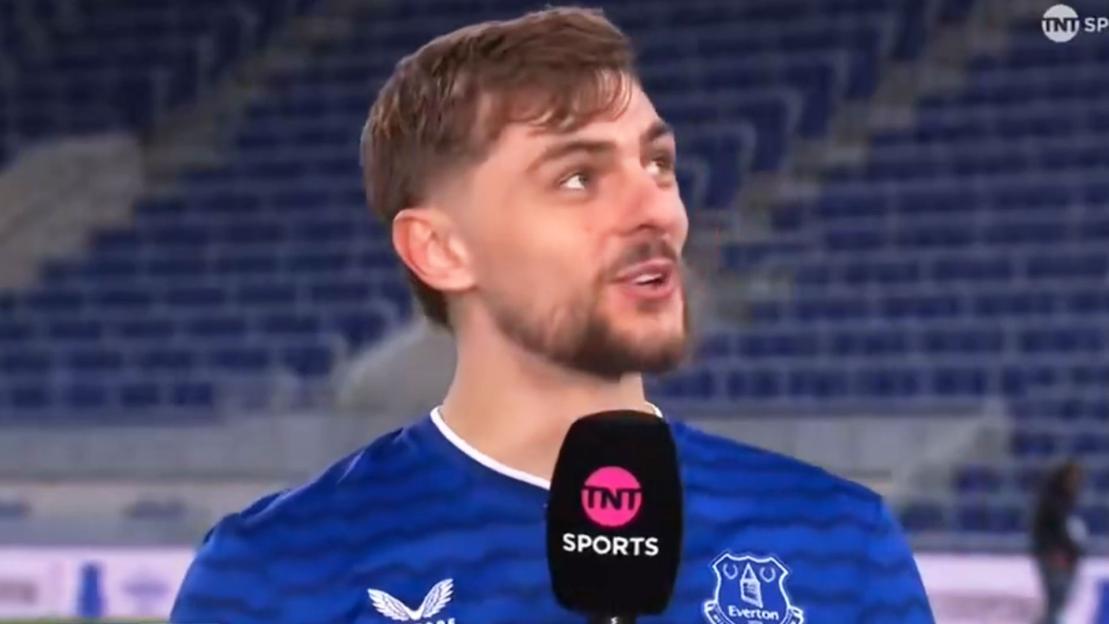 A man wearing an Everton jersey and a TNT Sports microphone looking up and to the right.