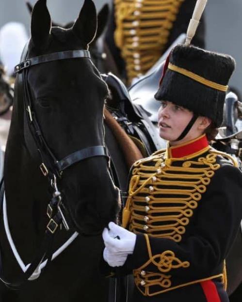 A woman in a military uniform with gold braiding pets a black horse.