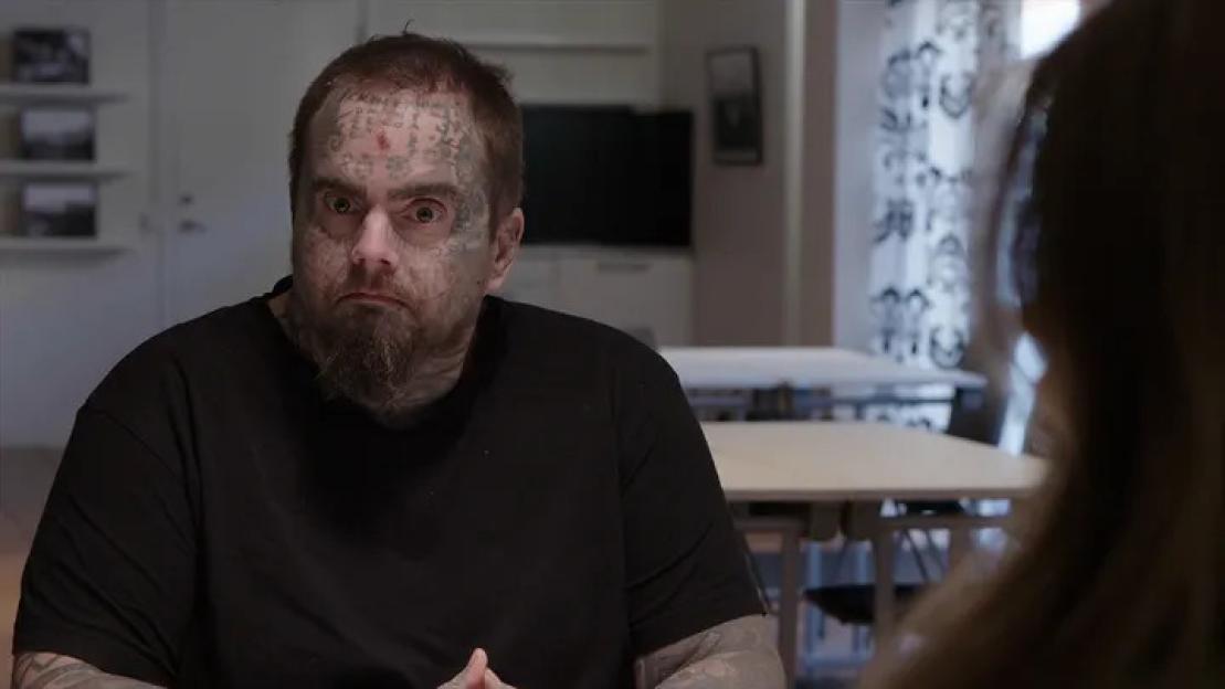 Isakin Jonsson, a man with a beard and tattoos on his face, neck, and arms, looks forward with wide eyes.