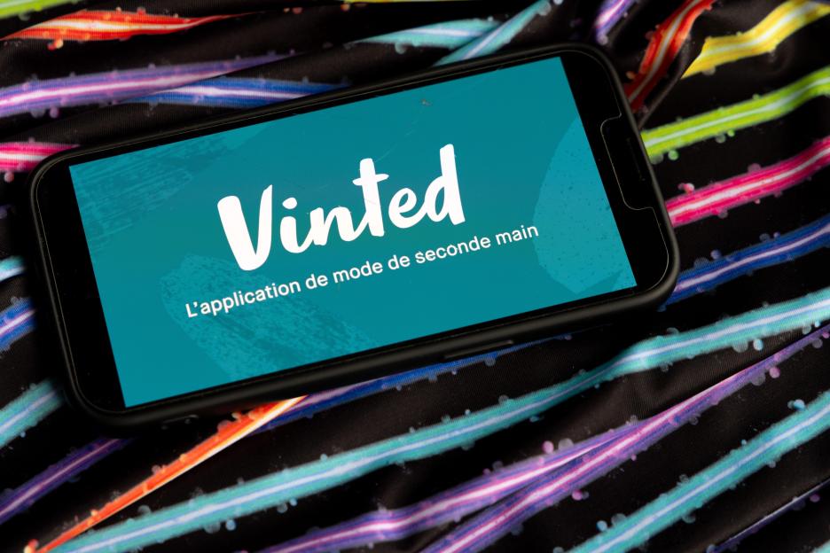 An iPhone displays the Vinted logo and slogan on a screen, resting on colorful fabric.