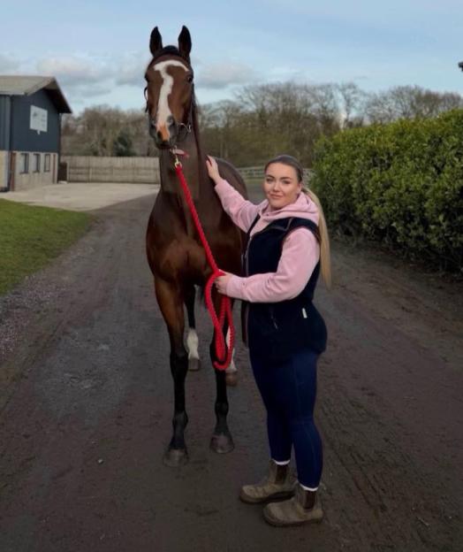 Hannah Bloor, a horsewoman, poses with a brown horse.