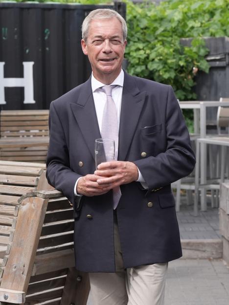 Nigel Farage, leader of Reform UK, standing outdoors with a drink in his hand.