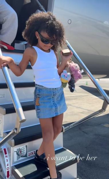 Stormi Webster descending airplane stairs, holding plush Labubu toys.