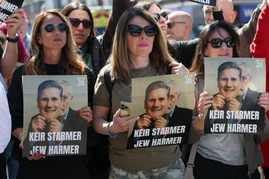 People hold signs protesting British Prime Minister Keir Starmer.
