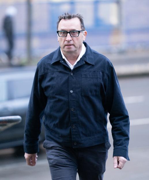 Gareth Lloyd walking, wearing a dark jacket, white shirt, and glasses.