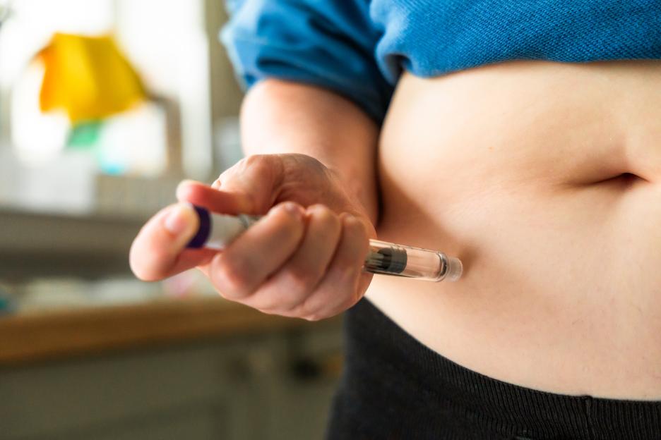 Woman using an injection pen to administer a weight loss drug into her abdomen.