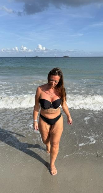 Katie Bailey in a black bikini walking out of the ocean.
