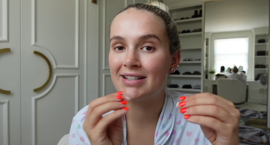 A woman in a striped pajama top with her hair in a bun gestures with her hands, showing off her bright orange manicured nails.