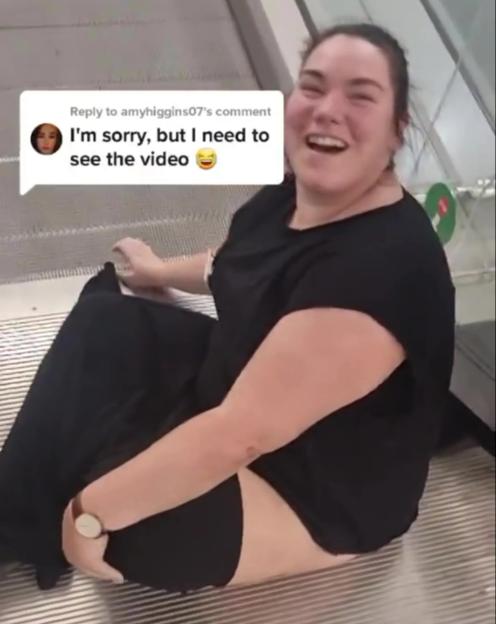 A woman laughing while sitting on an escalator step with her clothing caught.