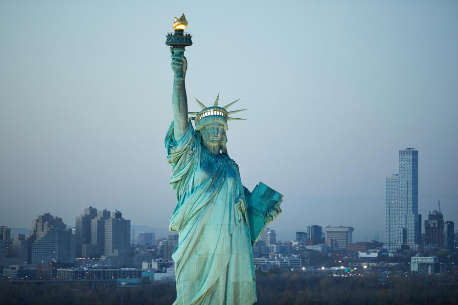 Aerial photo of the Statue of Liberty at sunset with Jersey City in the background.