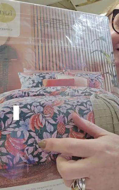 A person holds up packaged bedding featuring a pattern of pineapples, bananas, and flowers.