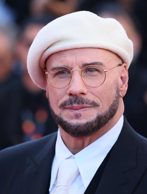 John Travolta wearing a white beret, glasses, and a black suit at the Cannes Film Festival.