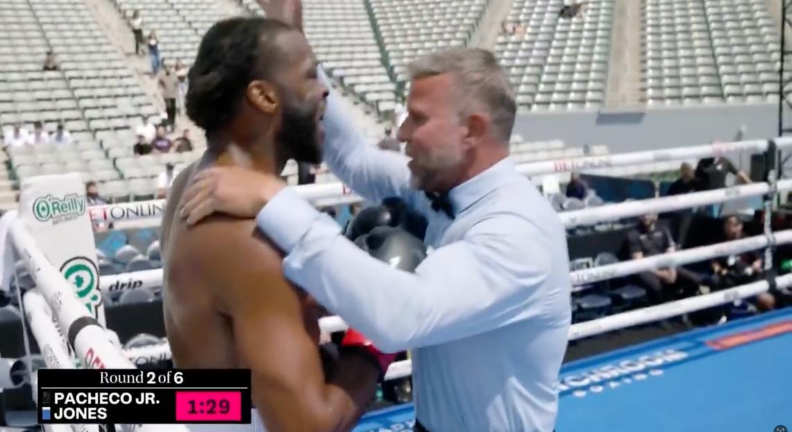 A referee separating two boxers in a boxing ring during Round 2 of 6.
