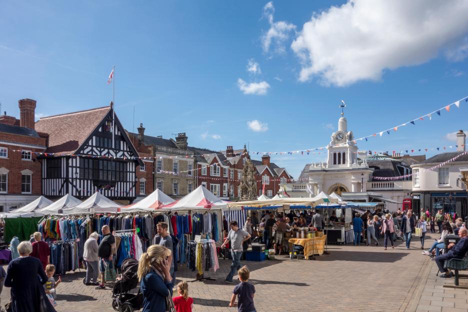 Saffron Walden Market in Essex, UK, with numerous stalls and shoppers, under a clear sky.