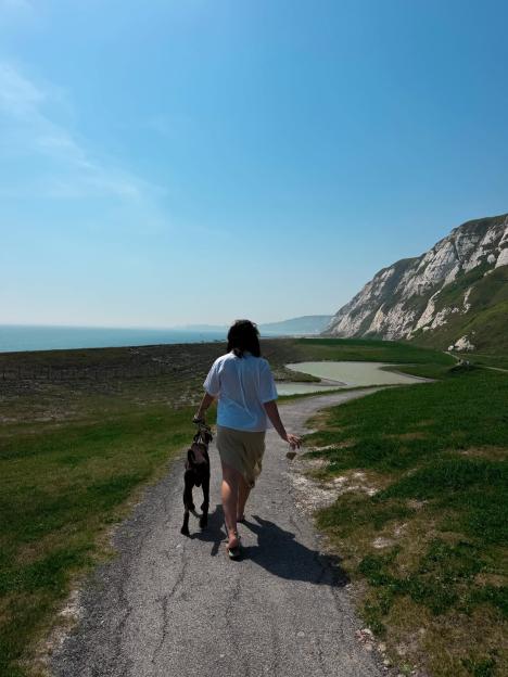 A person walks a dog on a path overlooking the sea and white cliffs.