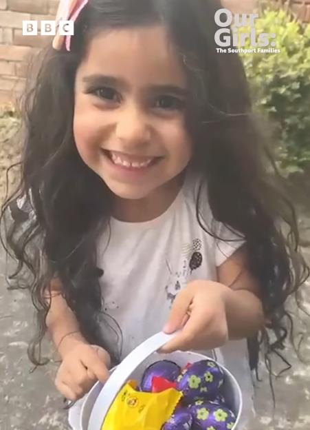 A smiling girl holds a bucket of chocolate Easter eggs and candy.