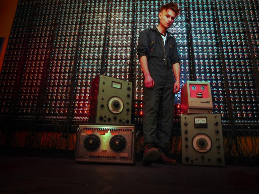 Youtuber and experimental singer/songwriter Look Mum No Computer stands among synthesizers and vintage computers.
