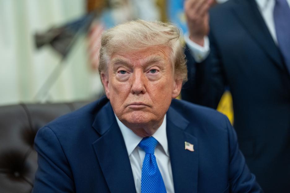Donald Trump sitting at a desk with an American flag pin on his lapel.