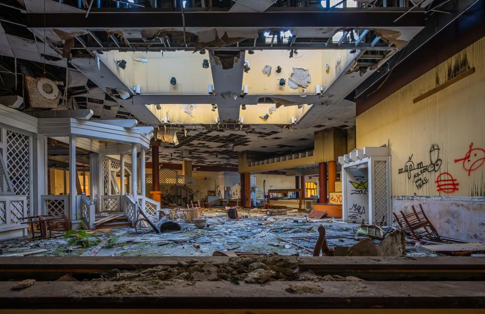The dilapidated interior of an abandoned hotel resort with a collapsed ceiling and debris-strewn floor.