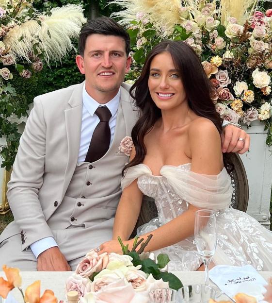 Fern and Harry Maguire smiling while seated at a table decorated with flowers and pampas grass.