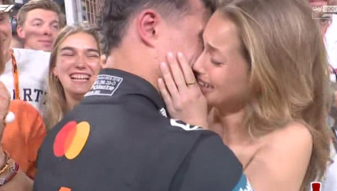 A woman embracing a man, crying tears of joy as people cheer in the background.