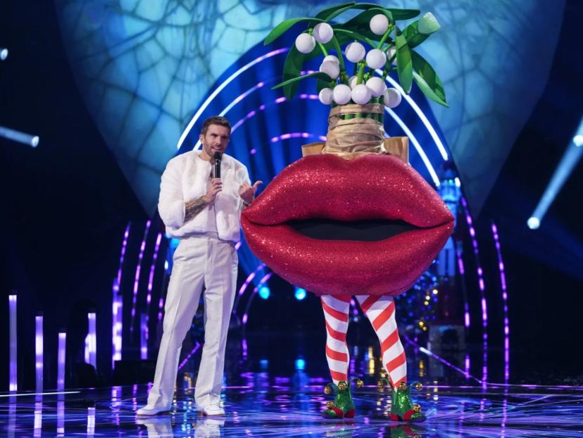 Joel Dommett interviewing a contestant dressed as a giant pair of glittery red lips with mistletoe.