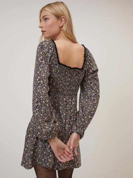 A woman models a black floral dress with a square neckline, long sleeves, and a shirred bodice.