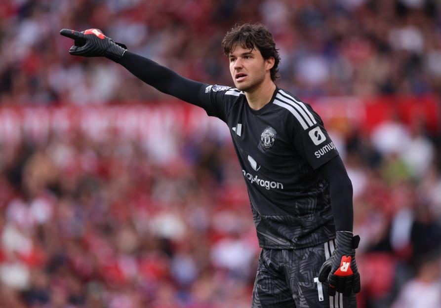A Manchester United goalkeeper in a black uniform with a red glove on his left hand pointing to the left during a Premier League match.