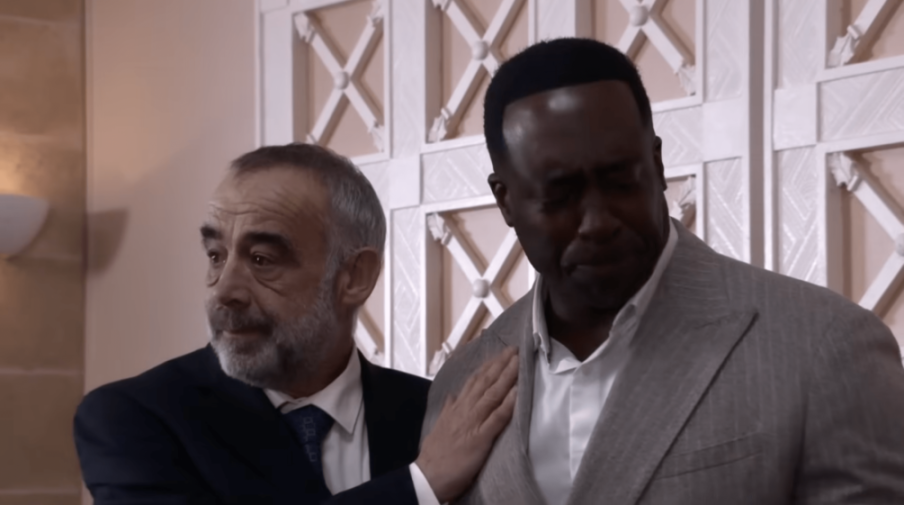 A man in a suit places a comforting hand on another man's shoulder.