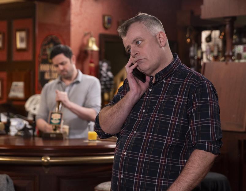 Steve McDonald, played by Simon Gregson, speaks on the phone in a pub.