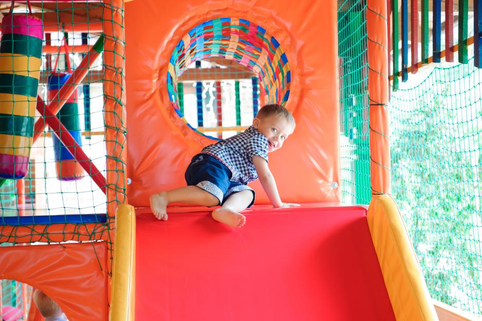 Toddler boy crawling in a colorful indoor playground.