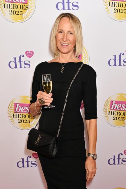 A woman in a black dress holding a glass of champagne, smiling at the "Best Heroes Awards 2025."