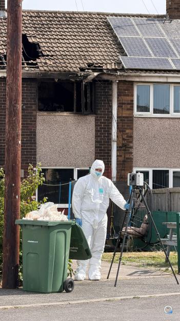 Police in protective suits investigating a house fire.