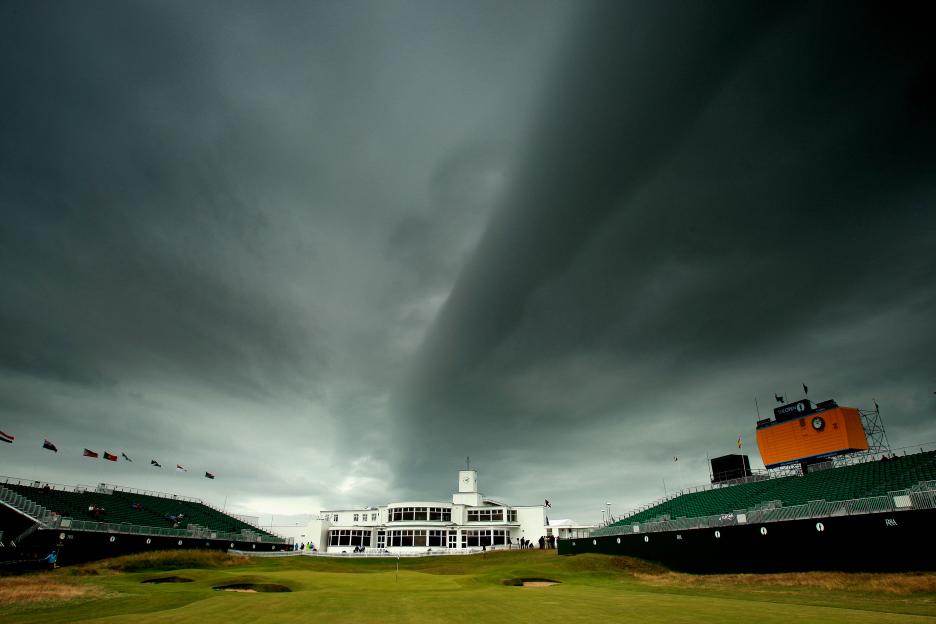 The 18th green at Royal Birkdale Golf Club with the clubhouse and grandstands under dark, stormy skies.