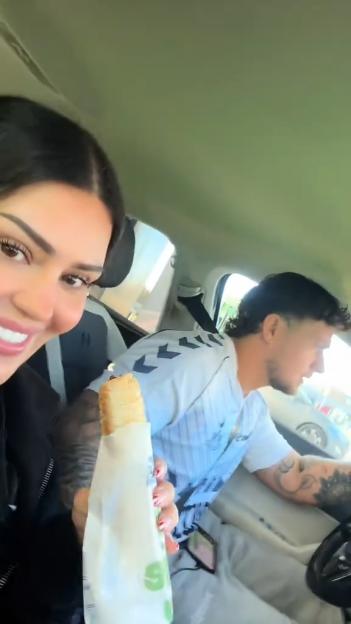 Woman in a car holding a Subway sandwich, with a man driving next to her.