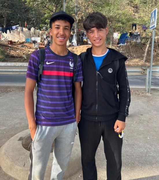 Mohammed Achaoui and Billal Boudamei, two migrants, smiling in front of a makeshift refugee camp in Ceuta.