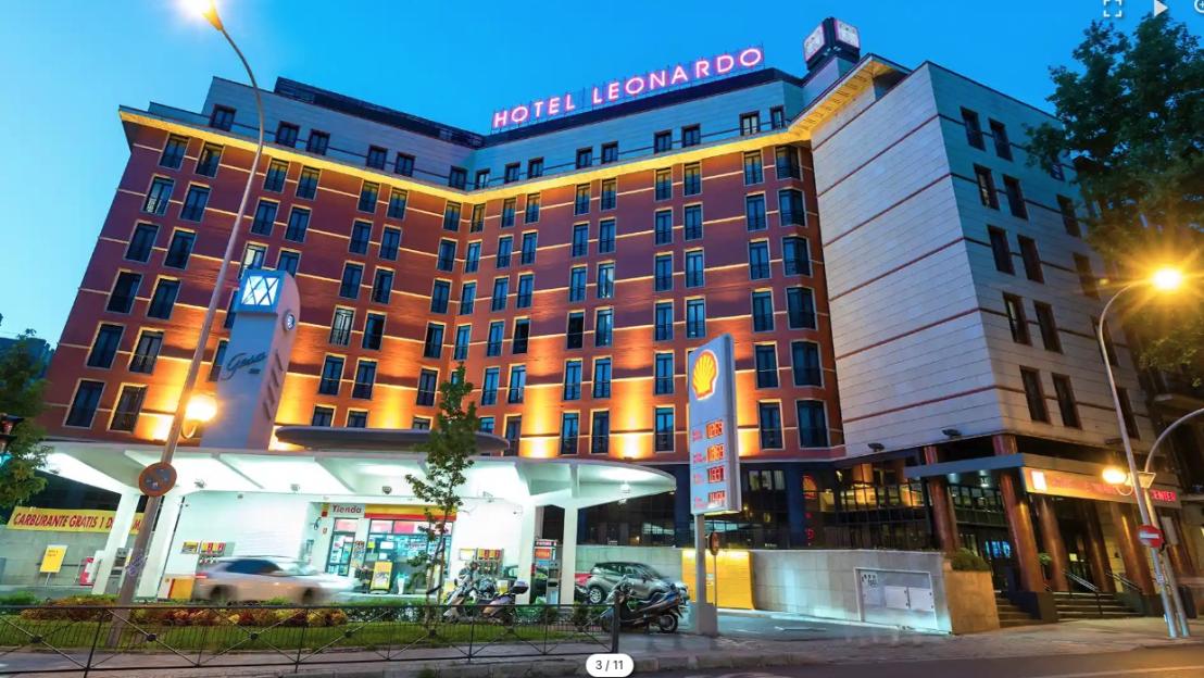 The Leonardo Hotel Madrid City Center at dusk, illuminated by orange lights, with a Shell gas station in front.