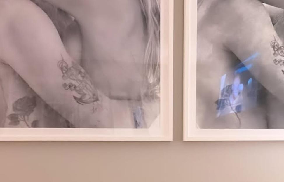 Wall art of partially visible figures with tattoos, framed in white.