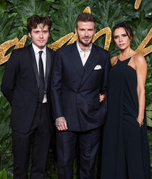Brooklyn Beckham, David Beckham, and Victoria Beckham pose on a red carpet.
