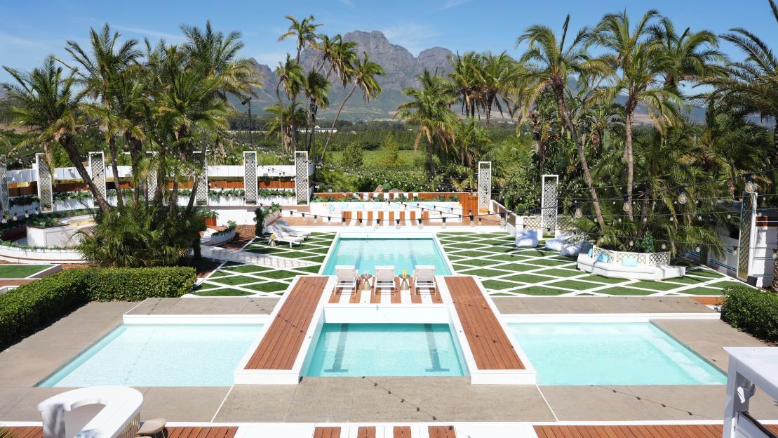 The luxurious outdoor villa for Love Island All Stars, with multiple swimming pools, lounge areas, and palm trees against a mountainous backdrop.
