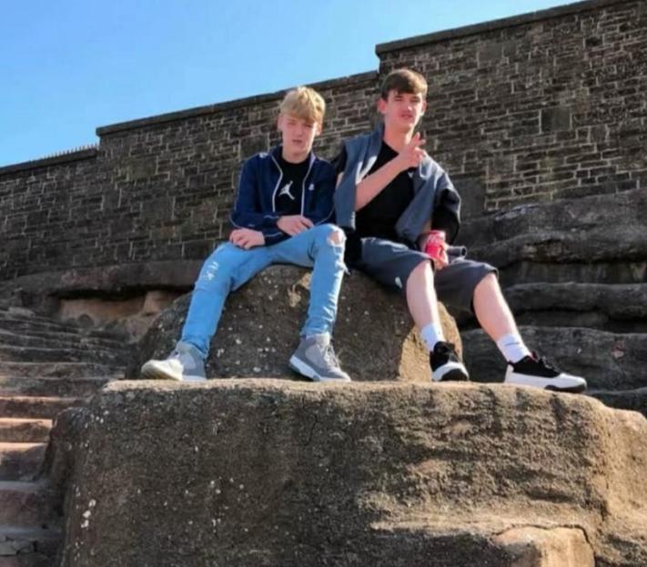 Two young men sitting on large rock steps under a clear blue sky.